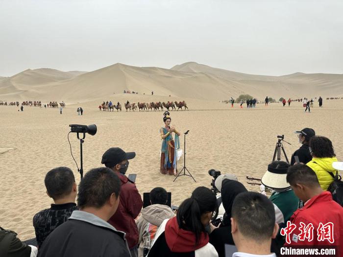 圖為2023年4月底，敦煌大漠“逐舞者”奧楠在鳴沙山月牙泉景區(qū)視頻直播，吸引游人圍觀?！●T志軍 攝